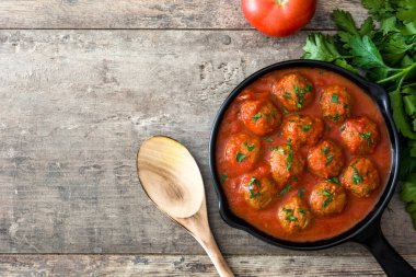 Meatballs with tomato sauce in iron frying pan on wooden table. Top view clipart