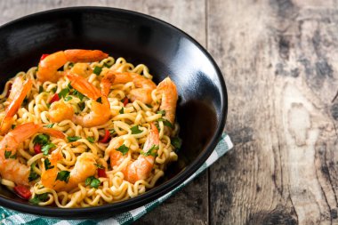 Erişte ve ahşap masa üzerinde siyah kase sebzeli karides