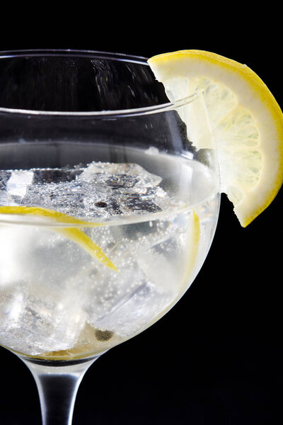 Glass of gin tonic with lemon on black stone background