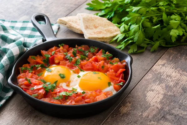 Shakshuka in iron frying pan on wooden table. Typical food in Israel. — Stock Photo, Image
