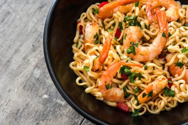 Erişte ve ahşap masa üzerinde siyah kase sebzeli karides