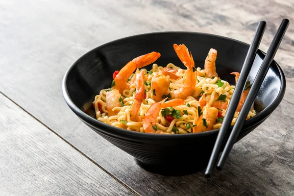 Noodles and shrimps with vegetables in black bowl on wooden table — Stock Photo, Image