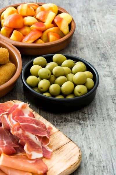 Tapas tradicionales españolas. Croquetas, aceitunas, tortilla, jamón y patatas bravas sobre mesa de madera — Foto de Stock