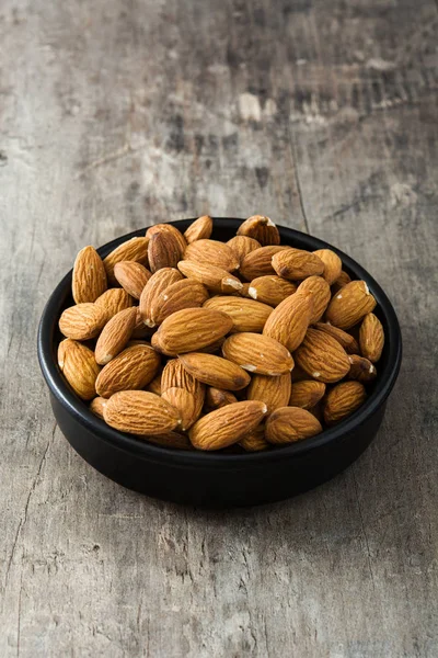 Almendras en tazón negro sobre mesa de madera — Foto de Stock