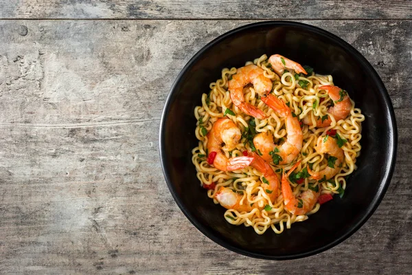 Erişte ve ahşap masa üzerinde siyah kase sebzeli karides