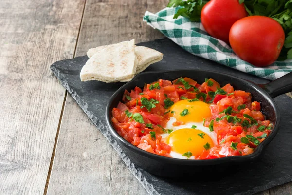 Ahşap masa üzerinde demir tavada Shakshuka. İsrail geleneksel yemekler.