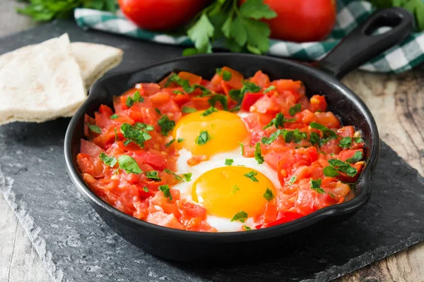 Ahşap masa üzerinde demir tavada Shakshuka. İsrail geleneksel yemekler.