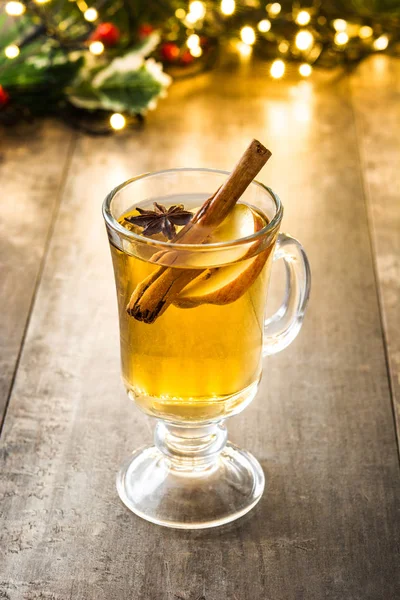 Mulled cider in glass, ornaments and christmas light on wooden table — Stock Photo, Image