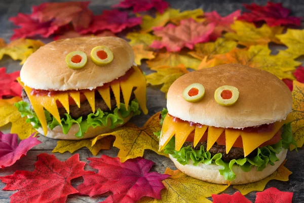 Monstros de hambúrguer de Halloween na mesa de madeira e folhas de outono — Fotografia de Stock