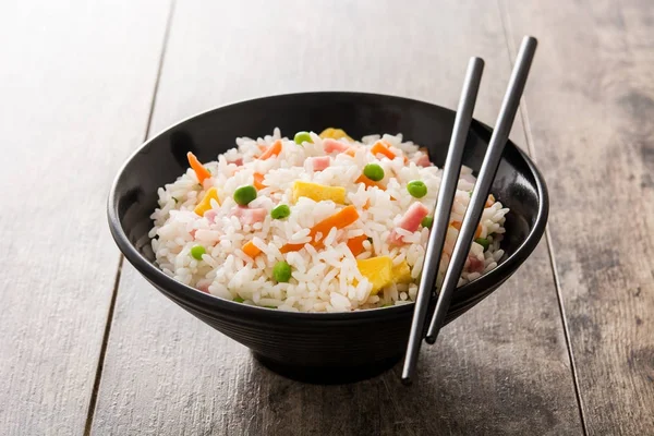 Жареный рис с овощами и омлетом в черной миске на деревянном столе — стоковое фото
