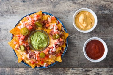 Sığır eti, guacamole, peynir sos, biber, domates ve soğan ahşap masa üzerinde plaka ile Meksika Nacho. Üstten Görünüm