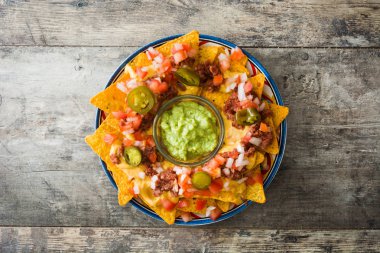 Sığır eti, guacamole, peynir sos, biber, domates ve soğan ahşap masa üzerinde plaka ile Meksika Nacho. Üstten Görünüm