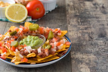 Sığır eti, guacamole, peynir sos, biber, domates ve soğan ahşap masa üzerinde plaka ile Meksika cips