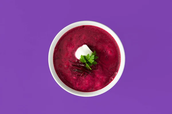 Beet soup in white bowl isolated on purple background. Top view