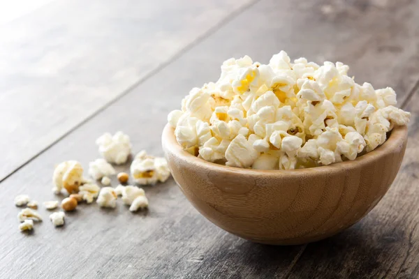 Popcorn in bowl on wooden table.