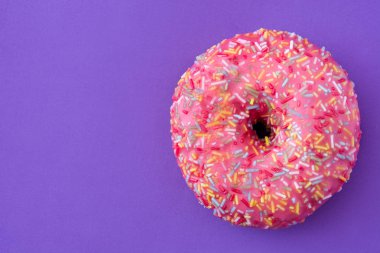 Menekşe arka plan üzerinde renkli sprinkles ile pembe buzlu çörek. Üstten Görünüm. Boşaltmak