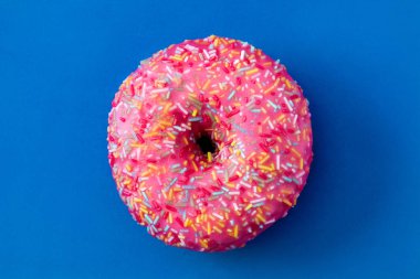 Menekşe arka plan üzerinde renkli sprinkles ile pembe buzlu çörek. Üstten Görünüm.