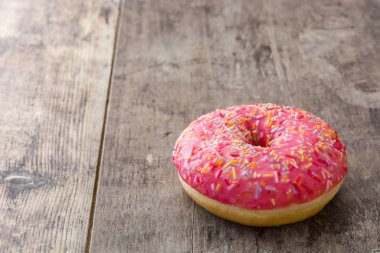 Ahşap masa üzerinde renkli sprinkles ile pembe buzlu çörek