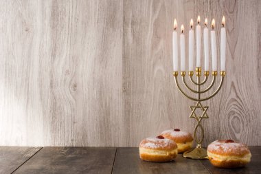 Jewish Hanukkah menorah and sufganiyot donuts on wooden table. Copy space