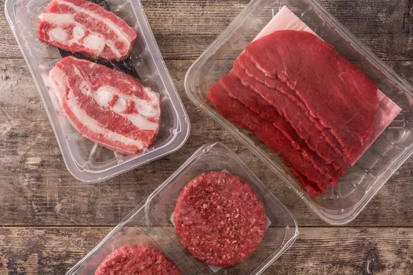 Different types of meat packaged in plastic on wooden table. Top view