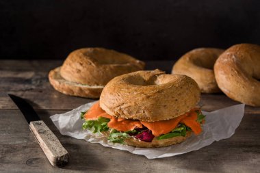 Krem peynirli bagel sandviç, füme somon ve ahşap masada sebze.