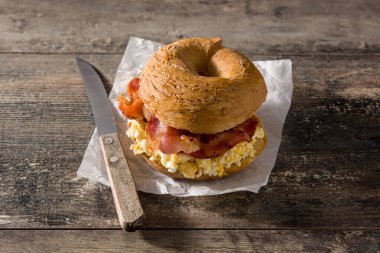 Pastırmalı simit sandviç, ahşap masada yumurta ve peynir.