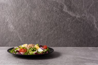 Ton balıklı salata, yumurta ve sebzeler gri arka planda. Boşluğu kopyala