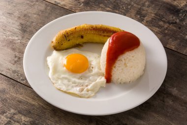Arroz a la cubana Tipik Küba pirinci kızarmış muz ve kızarmış yumurta ile ahşap bir tabakta. 