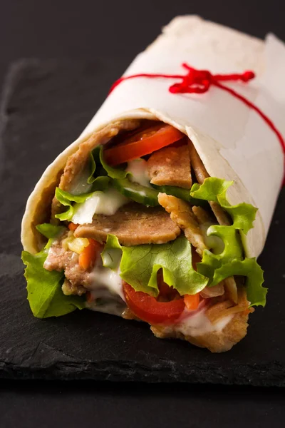 Doner kebab or shawarma sandwich on black slate background. Close up