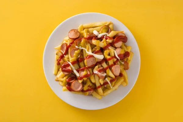Typical Latin America Salchipapa on yellow background. Sausages with fries, ketchup,mayo and mustard.