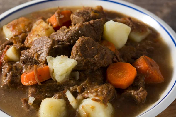 Irish beef stew with carrots and potatoes on wooden table. Close up