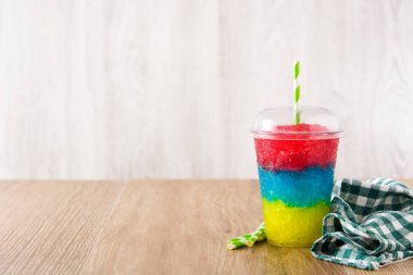 Farklı aromalı renkli buzlu içecek. Tahta masada plastik bardakta saman var. Boşluğu kopyala