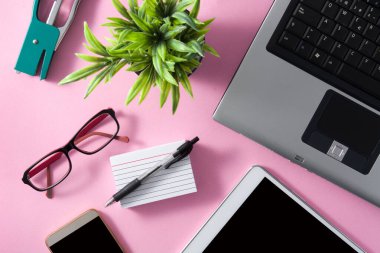Pembe arka planda bilgisayar, tablet ve akıllı telefonlu bir çalışma alanı konsepti. Üst görünüm