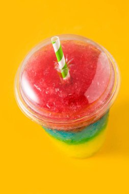 Colorful slushie of differents flavors with straw on yellow background clipart