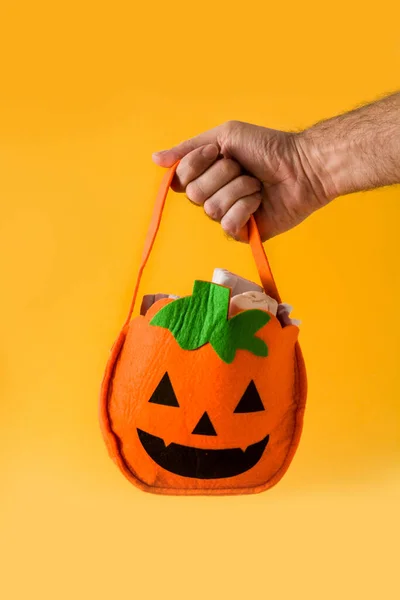 Hand holding Halloween pumpkin bag with candies inside isolated on yellow background