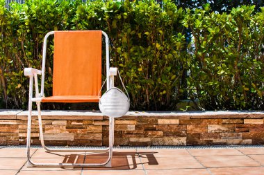 Koruyucu yüz maskesi ve ağaç manzaralı turuncu sandalye. Doğanın ortasında. Coronavirus COVID-19 döneminde kırsal tatiller