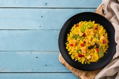 Kızarmış pilav, tavuk ve sebzeler mavi ahşap masada siyah tabakta. Üst Manzara. Boşluğu kopyala