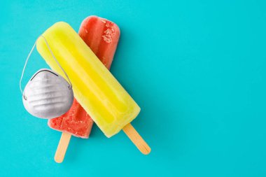 Mavi arka planda koruyucu yüz maskesi olan limonlu ve çilekli dondurma. Boşluğu kopyala