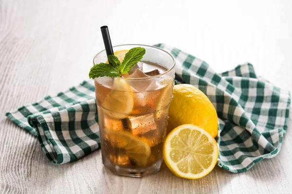 Iced tea drink with lemon in glass on white wooden table