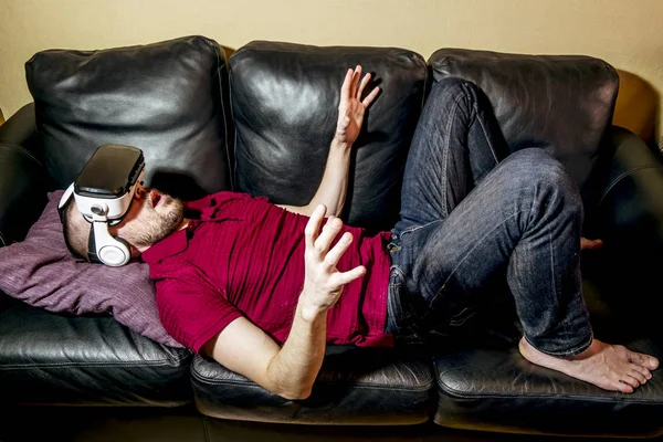 Mannen med brillene leker virtuell virkelighet på sofaen. – stockfoto