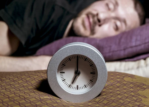 Clock standing on a pillow amid the sleeping men — Stock Photo, Image