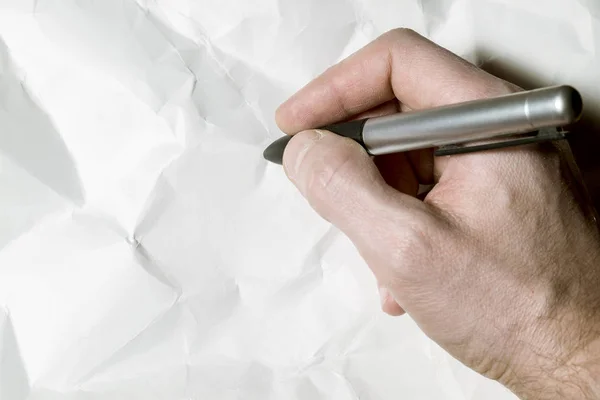 La main d'un homme écrit avec un stylo sur une feuille de papier froissé — Photo