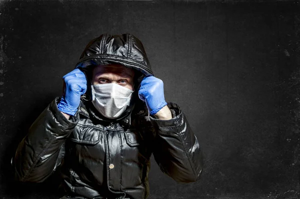 a man in a medical mask and gloves pulled his hood up against the dark background