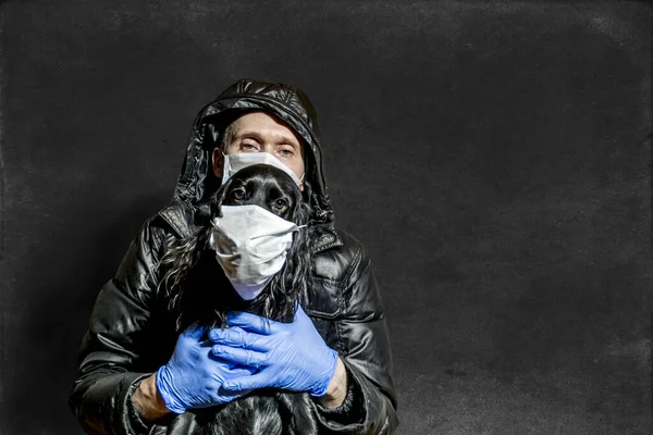 a man in a medical mask and gloves holds his dog in a medical mask on a dark background