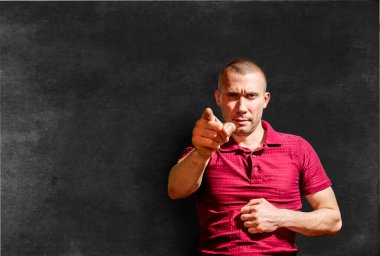 Sert görünüşlü bir adam işaret parmağıyla tahtaya işaret eder.