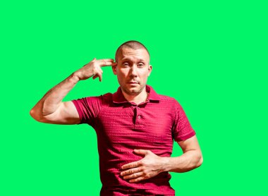 Adam yeşil bir arka planda, parmakları silah şeklinde olan elini kafasına koydu.