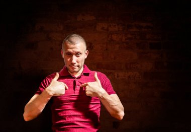 Kendinden emin bir adam işaret parmaklarıyla göğsünü tuğla duvara dayar.
