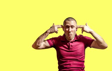 Adam sarı arka planda parmakları silah şeklinde olan ellerini kafasına koydu.