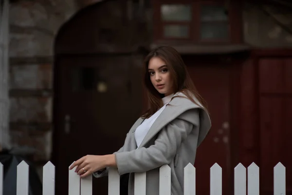Молода дівчина стоїть на тлі міської вулиці. Дівчинка в сірому пальто. Серія фотографій з брюнеткою — стокове фото