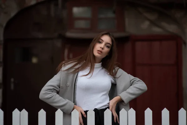 Giovane ragazza si trova sullo sfondo di una strada della città. Ragazza con un cappotto grigio. Una serie di foto con una bruna — Foto Stock